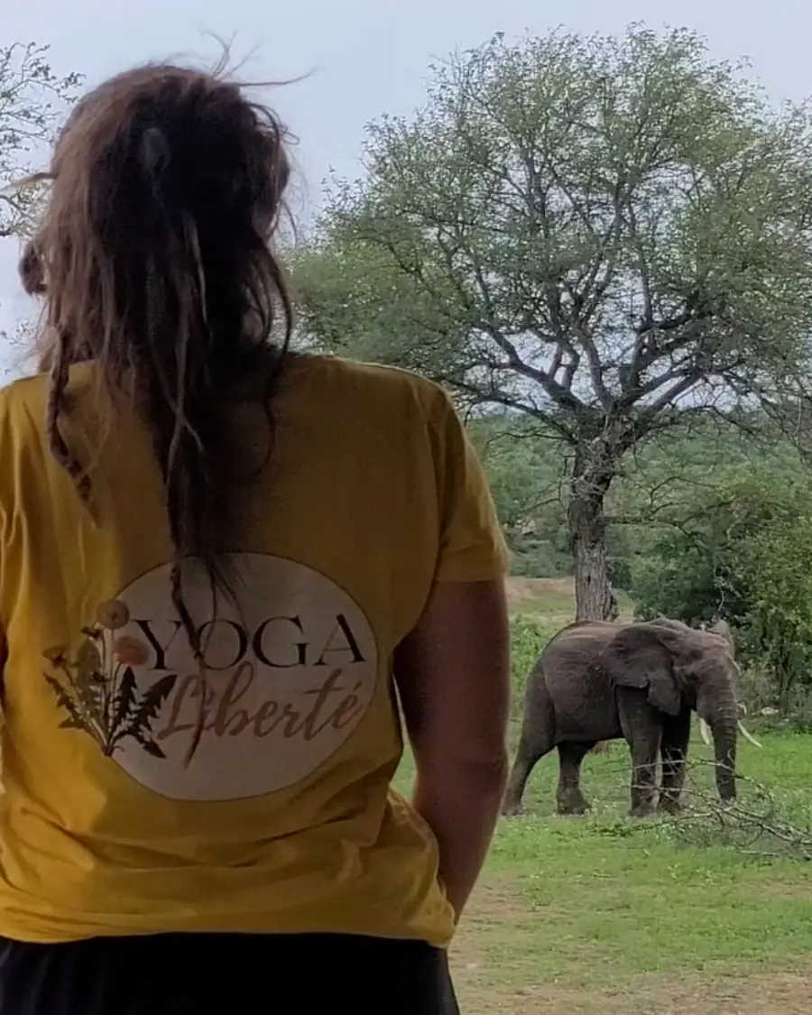 Pauline de dos, t-shirt Yoga Liberté, observe un éléphant dans le bush africain