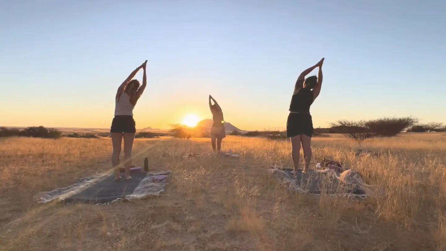 Silhouettes in yoga poses facing the setting sun in the African savannah