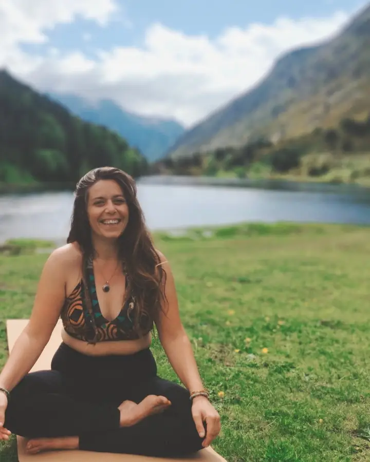 Pauline, souriante, assise en tailleur sur son tapis au bord d’un lac de montagne