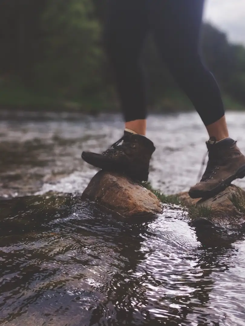 Les pieds de Pauline, en chaussures de randonnée, traversent une rivière de pierre en pierre