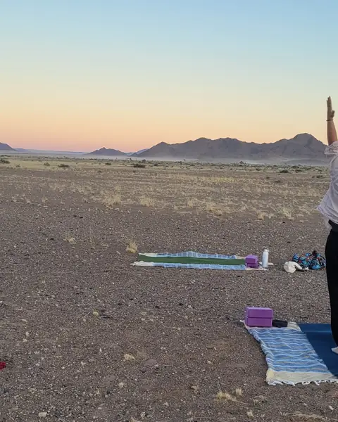 Two practitioners with arms raised on their mats, on a desert plain at sunset