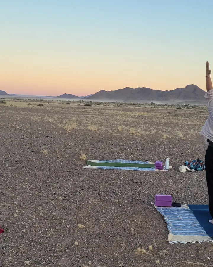 Deux pratiquantes bras levés sur leurs tapis, dans une plaine désertique au coucher du soleil