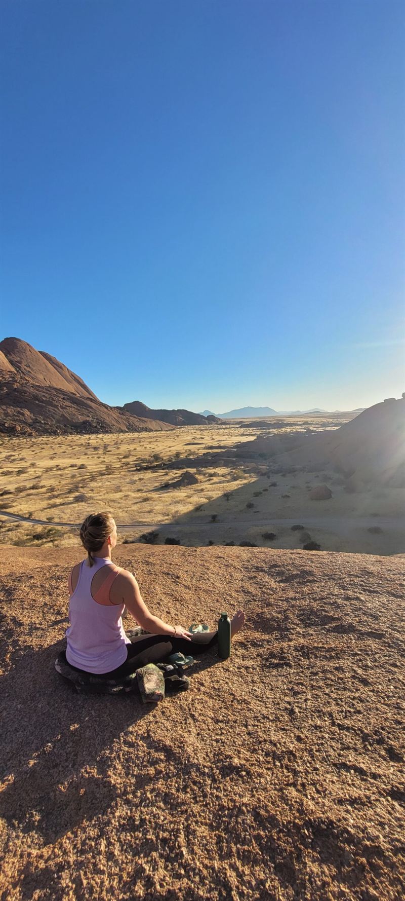 Une femme assise en méditation sur un plateau rocheux, face au soleil couchant