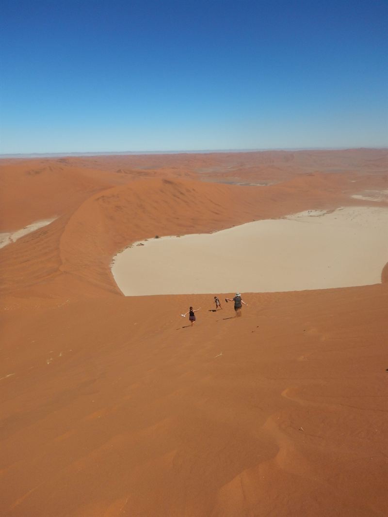 Vue aérienne de dunes rouges entourant une étendue blanche, avec quelques marcheurs