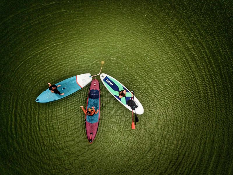 Trois paddles vus du ciel, sur une eau verte et calme