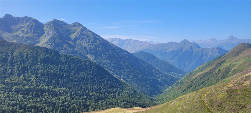 A panorama of green valleys and Pyrenean peaks under a blue sky
