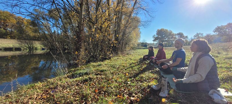 Un groupe en méditation dans l’herbe, au bord d’une rivière, sous le soleil d’automne