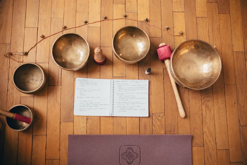 Des bols chantants posés sur un parquet en bois, près d’un tapis de yoga