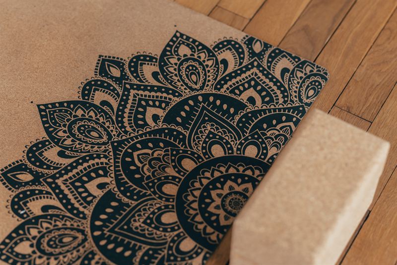 A mandala-print yoga mat and a cork block on the wooden floor