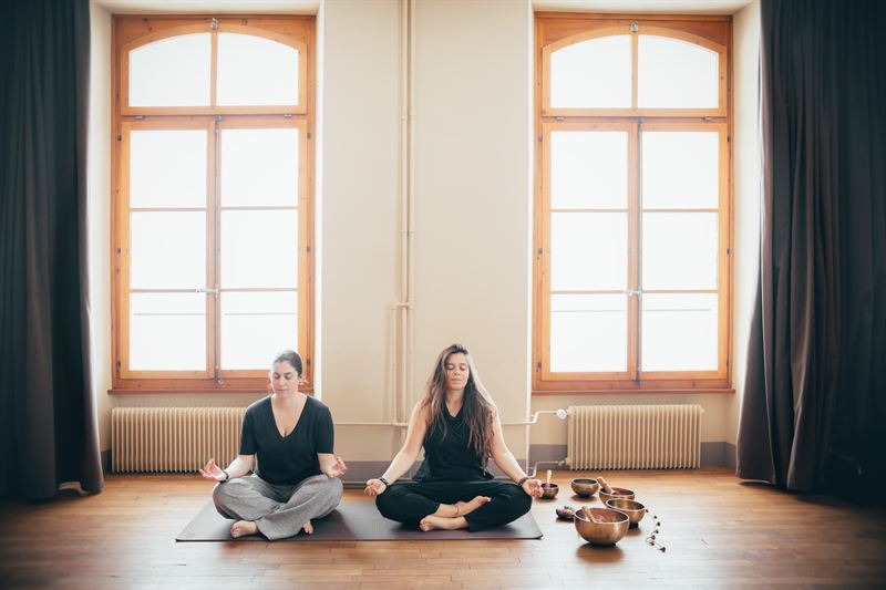 Two women meditating in the yoga room, facing the singing bowls