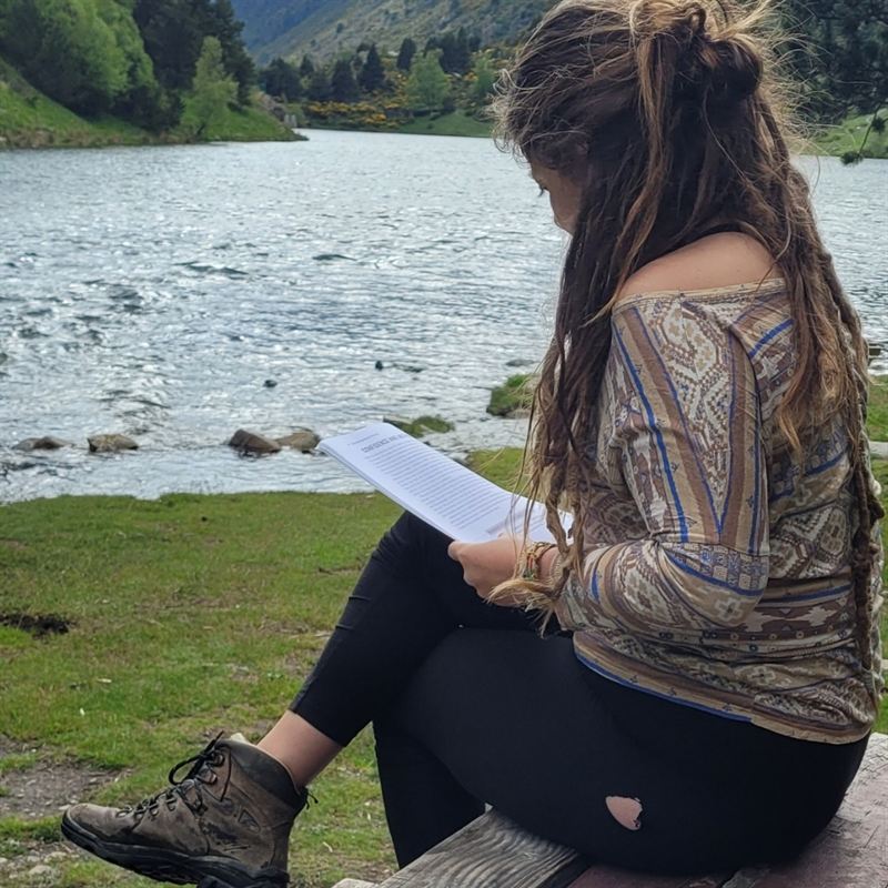 Pauline lit, assise au bord d’un lac de montagne, en chaussures de randonnée