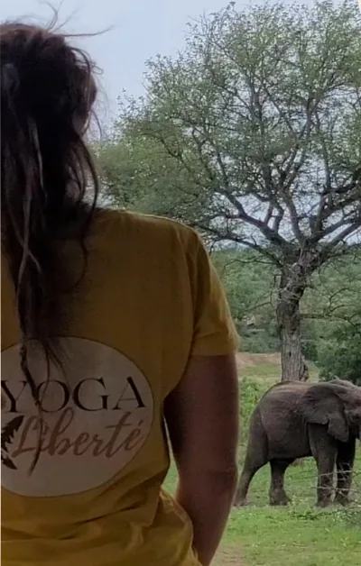 Pauline de dos, en t-shirt Yoga Liberté, face à un éléphant dans le bush
