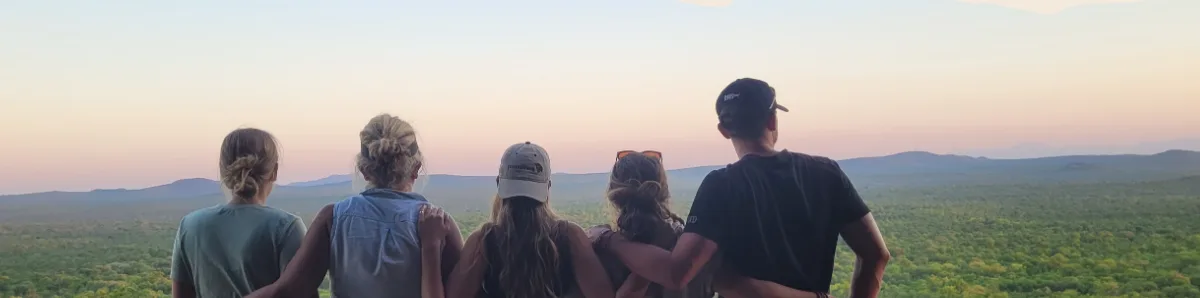 A group of travellers seen from behind, facing the savannah at sunset