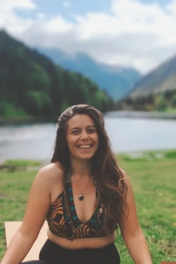 Pauline, souriante, assise en tailleur au bord d’un lac de montagne
